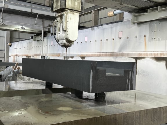 CNC-Bearbeitung eines nassen Granitblocks mit Brückenfräse – Werkstück wird auf Stahlträgern gehalten