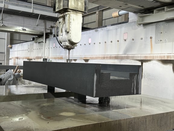 CNC-Bearbeitung eines nassen Granitblocks mit Brückenfräse – Werkstück wird auf Stahlträgern gehalten