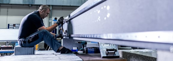 Mitarbeiter von REITZ Natursteintechnik montiert präzise Maschinenbau-Komponenten aus Granit mit modernem Equipment in der Produktionshalle.