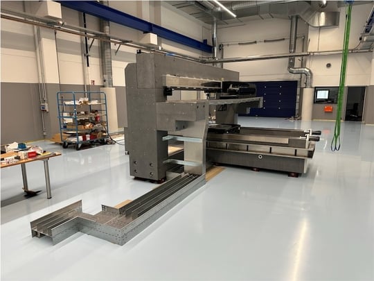 Motion-System mit sichtbarer Kabelführung und Linearachsen auf Granitstruktur – Maschinenaufbau in Produktionshalle